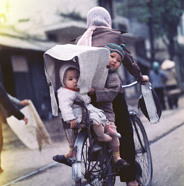 Hai em bé được mẹ chở bằng xe đạp trên phố.